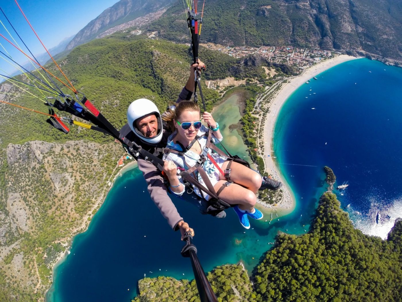 couple-of-people-flying-on-a-paraglide-over-the-turquoise-sea-and-beach-e1655888595491